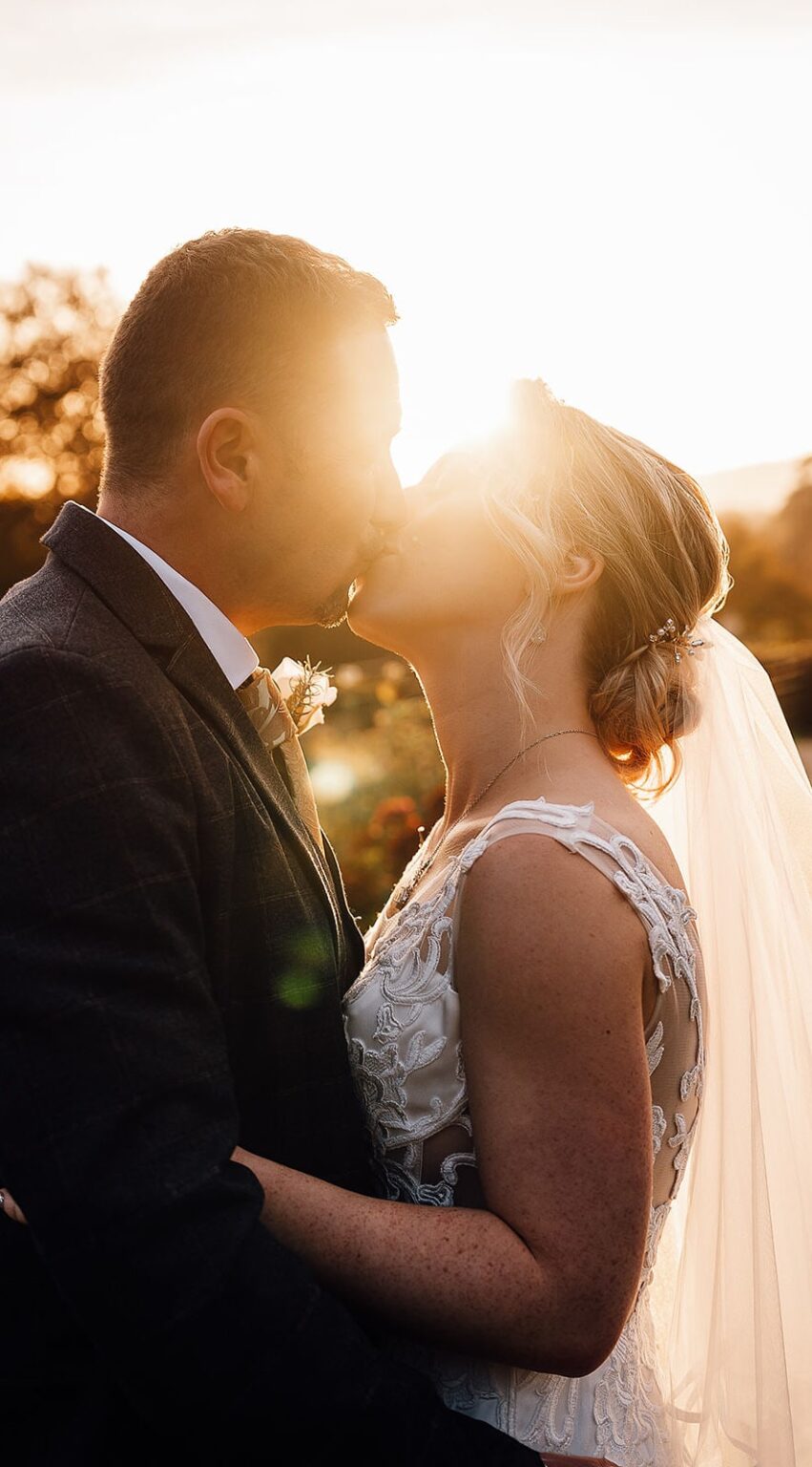 Bride and groom kiss with sun shining behind them
