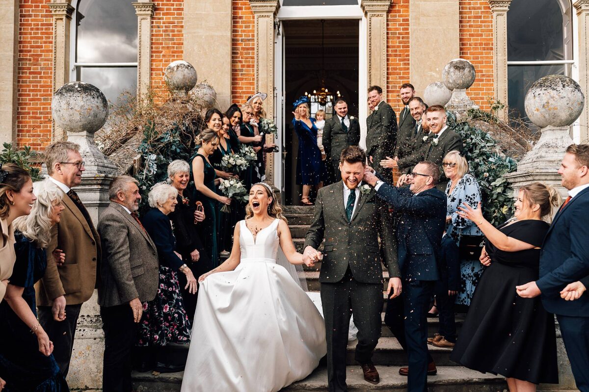 Newlyweds walk down the stairs outside Crowcombe Court as guests throw confetti at them