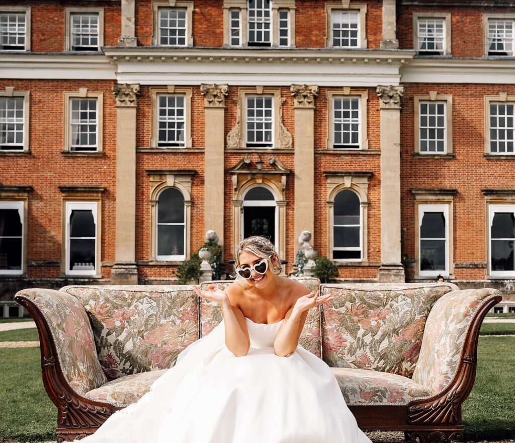 Bride sitting on sofa outside crowcombe court wearing sunglasses