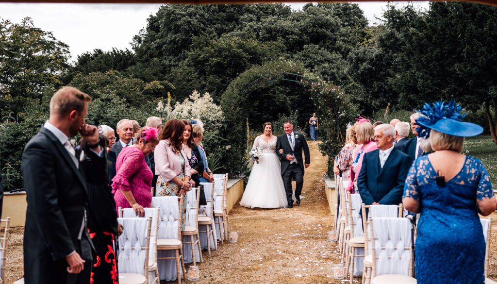 Bride walking down the aisle in an outdoors wedding ceremony at clevedon hall.