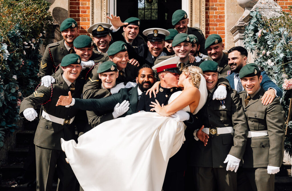 Wedding Photography Somerset Bride being picked up by the groom on Crowcombe court front steps while being surrounded by the grooms army soldier friends. Paul aston photography Somerset wedding Photographer