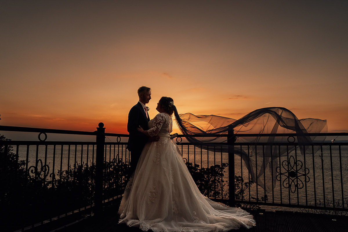 Bride and Groom standing on balcony of wedding venue Walton Park Hotel during sunset on their wedding day