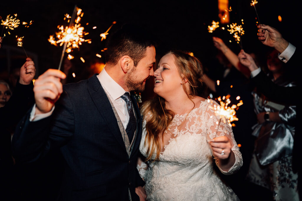 Bride and groom about to have a kiss while holding sparklers, surrounded by friends and family at their wedding.

