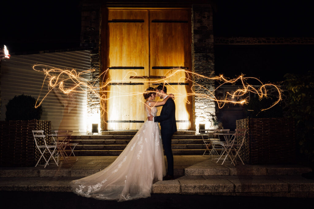 fun wedding ideas, Bride and groom posing in front of the great barn in devon, while people run around them sparklers making a cool light trail.