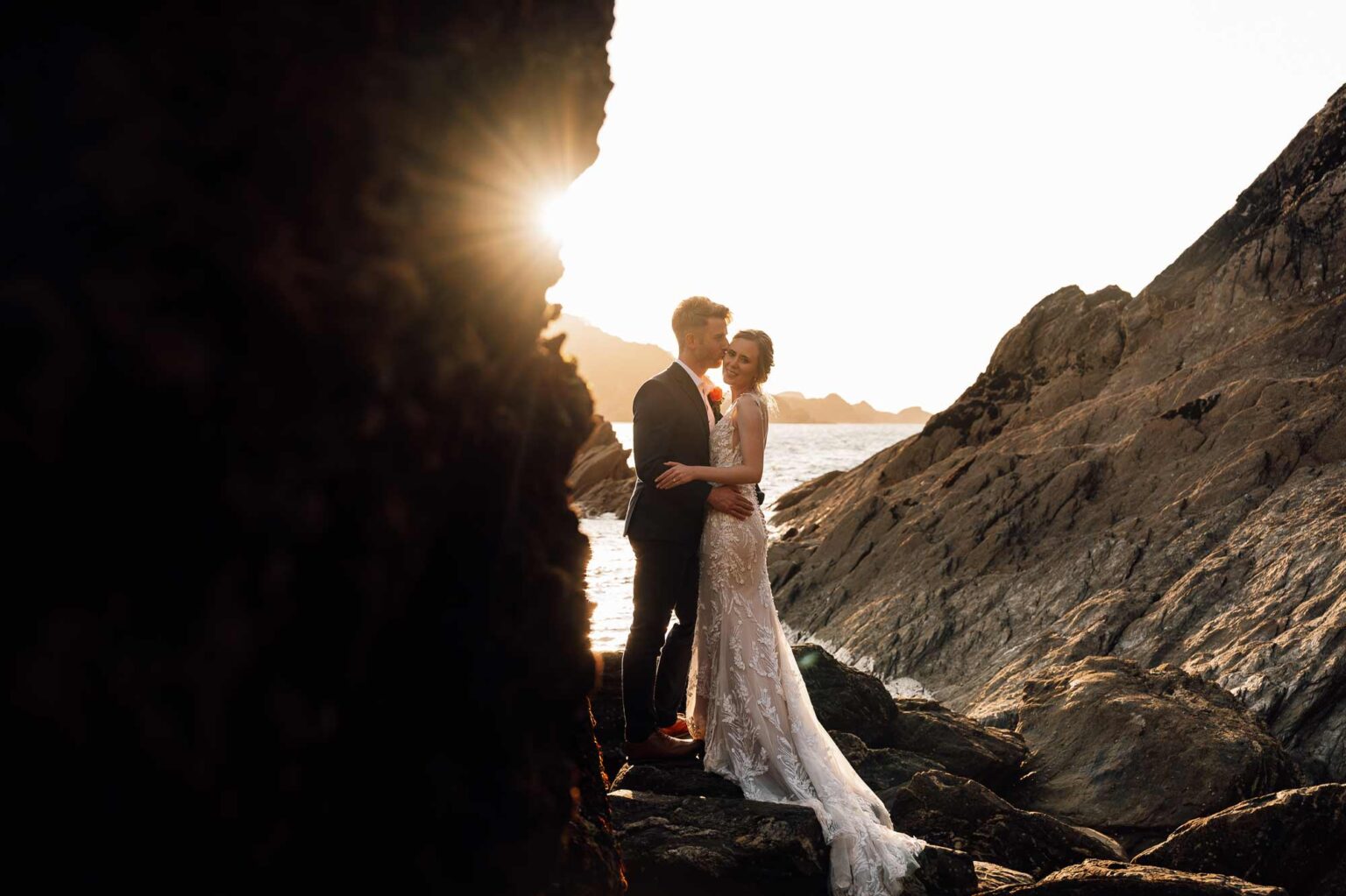 Coastal wedding photography with newlyweds stood with beautiful sunset