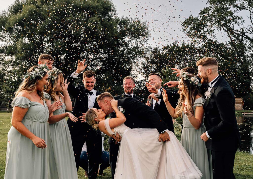 Bride and groom having a kiss in front of their bridal party at waterside country barn Wedding Photographer in Somerset - Paul Aston Photography