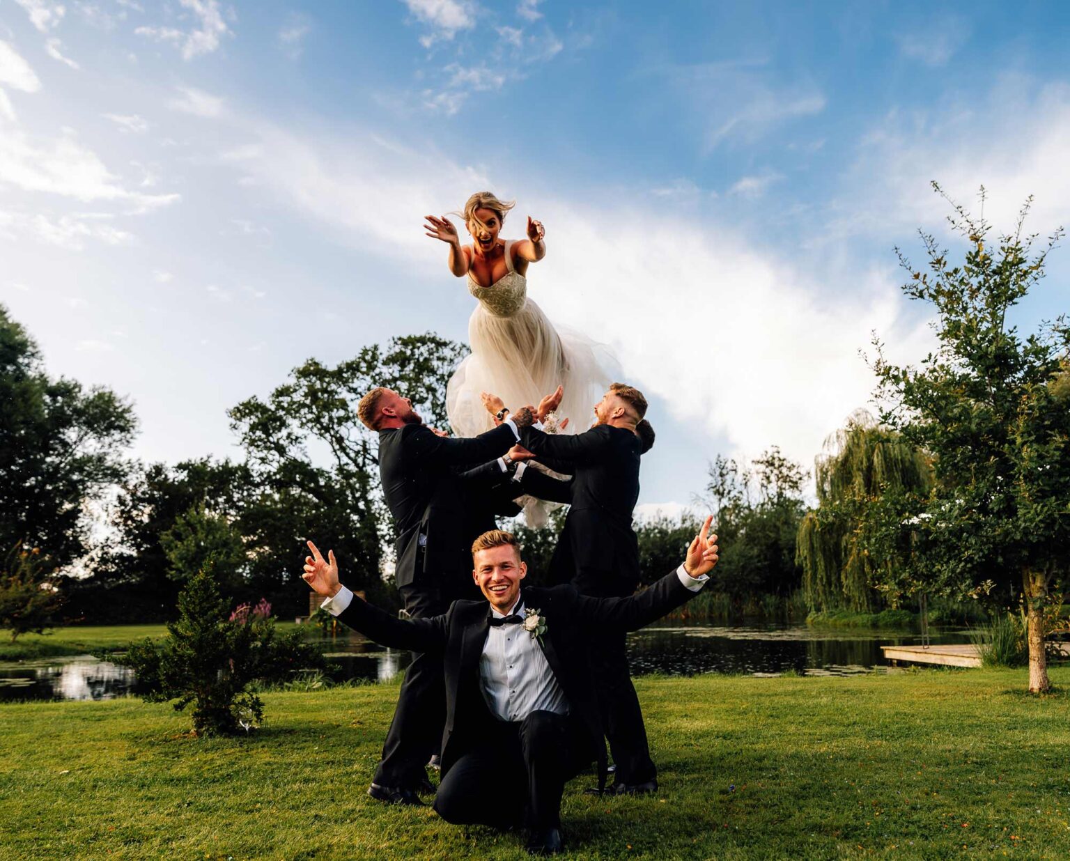 bride being chucked up in the air, with the groom sat in front looking all cool at waterside country barn Wedding Photographer in Somerset - Paul Aston Photography