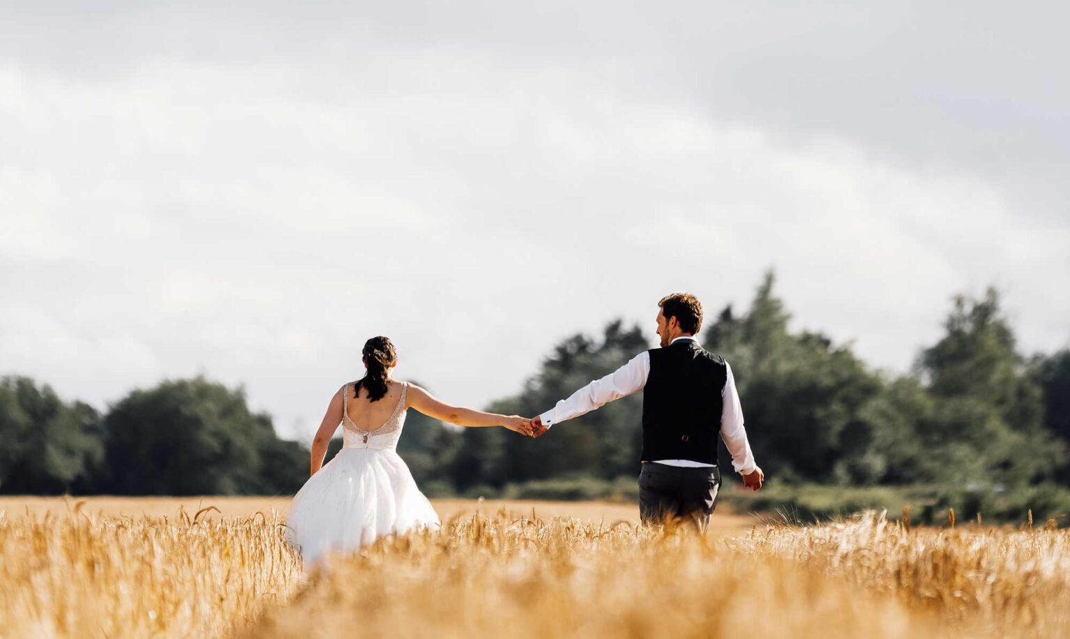 Married couple walk in fields of gold in Summer wedding