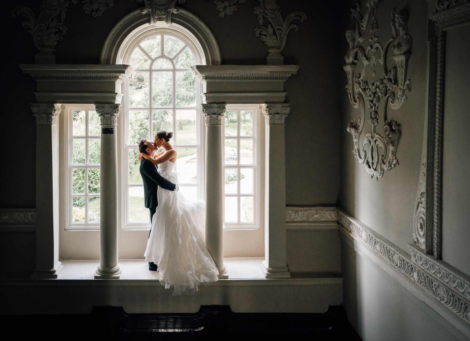 Kissing his wife, newlyweds embrace in wedding venue lovers window