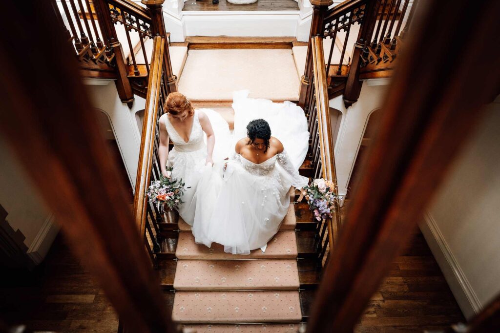 Lesbian wedding, both brides walk down the great stairs hand in hand at St audries wedding venue