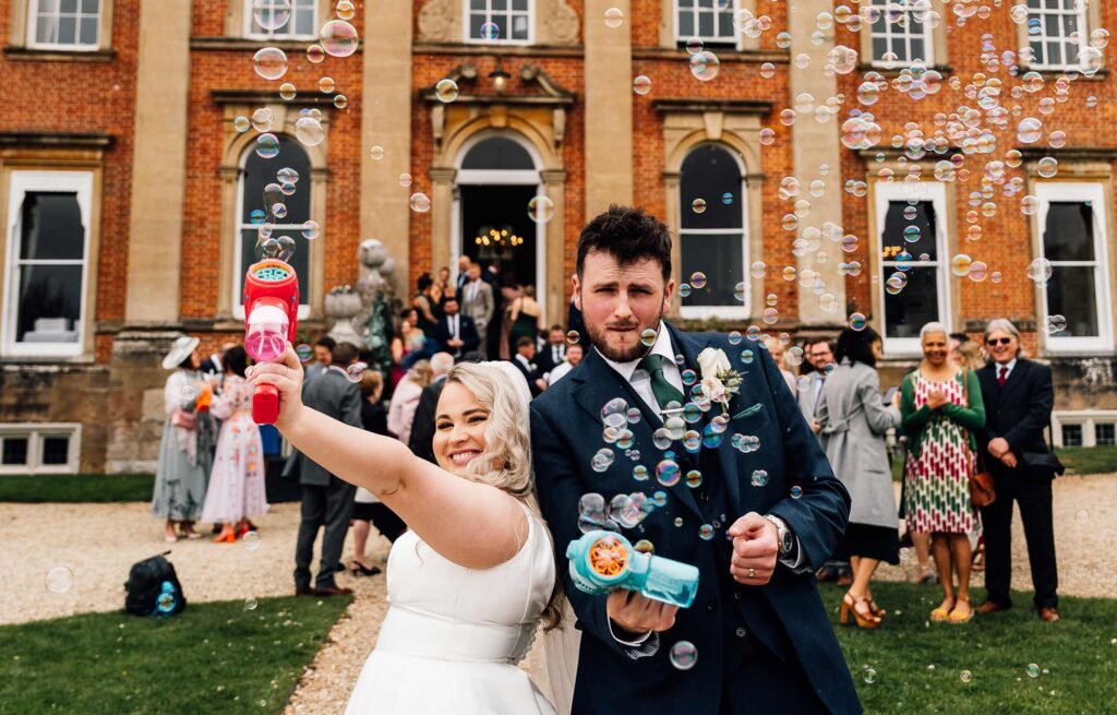 Bride and groom playing with bubble guns at their wedding with Crowcombe court behind them.